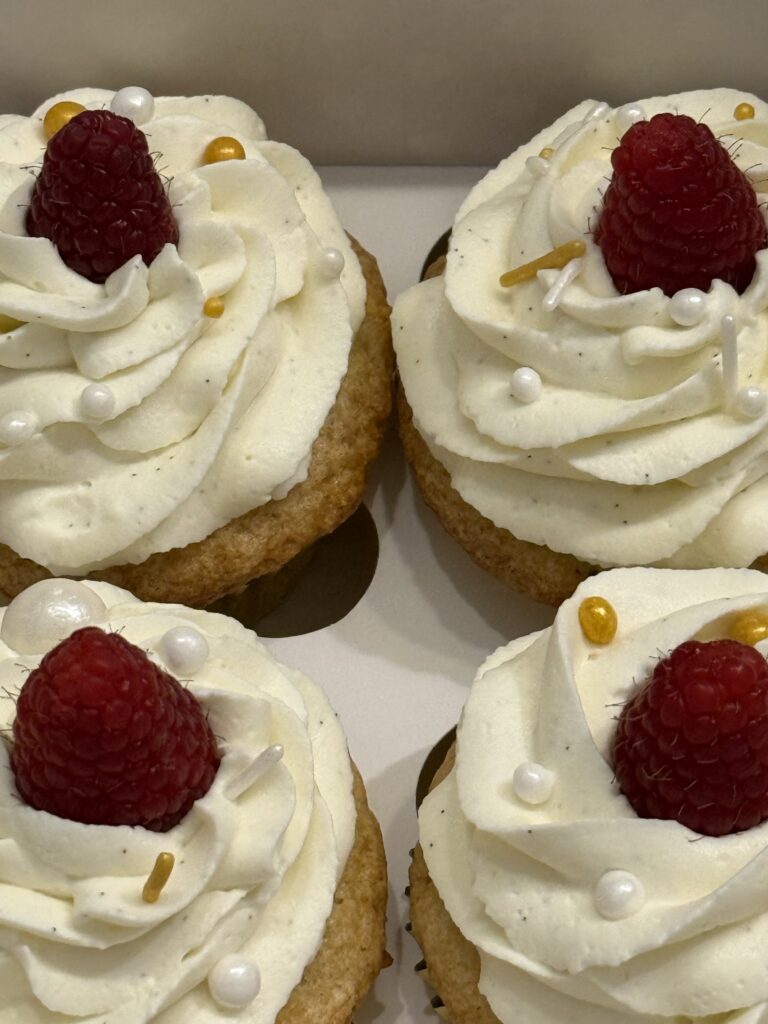 Gluten free vanilla cupcakes with raspberry filling and whipped vanilla bean frosting with a raspberry and sprinkles on top